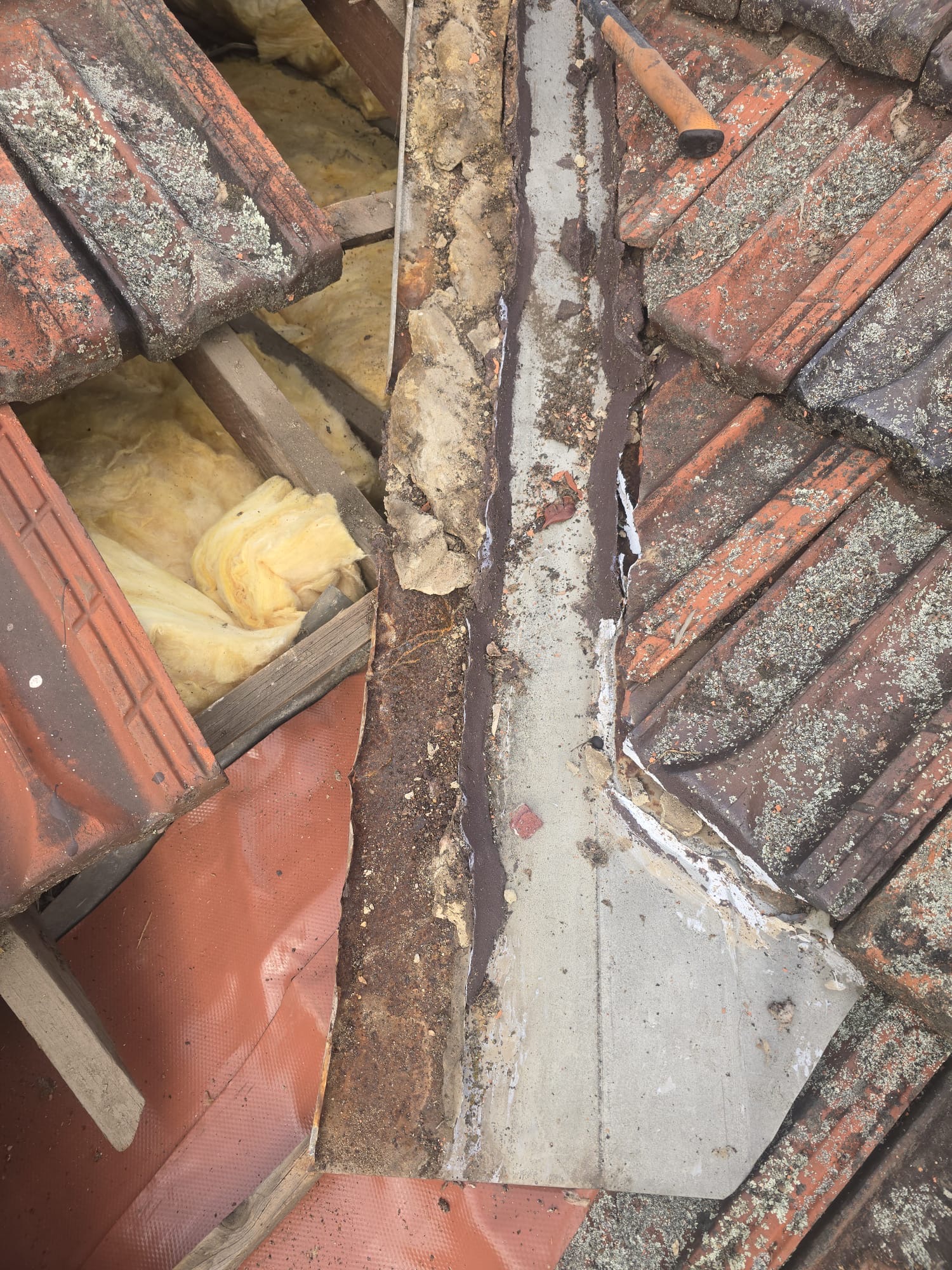 Terracotta tiles lifted to expose corrosion beneath mortar along the metal roof valley