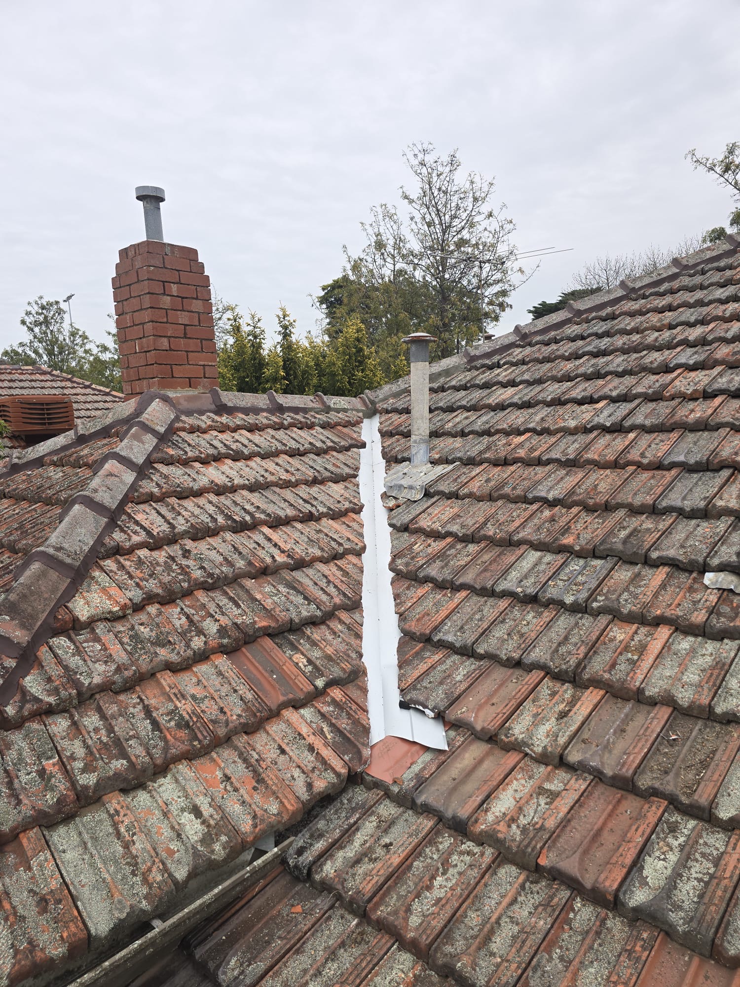 Replacement metal valley between terracotta roof slopes with an open watercourse