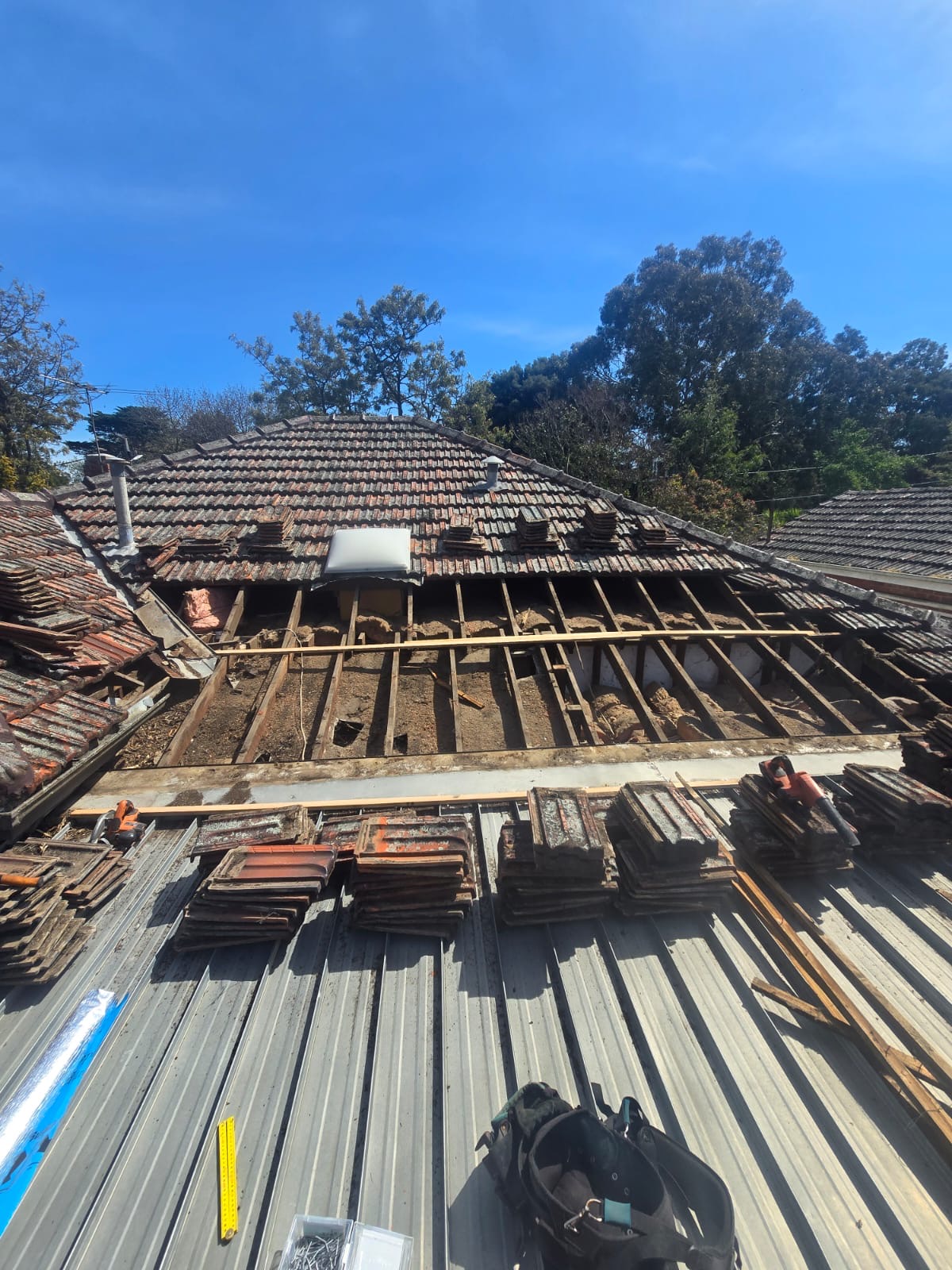 Skillion roof tiles removed, exposing timber framing without continuous sarking beneath the affected area