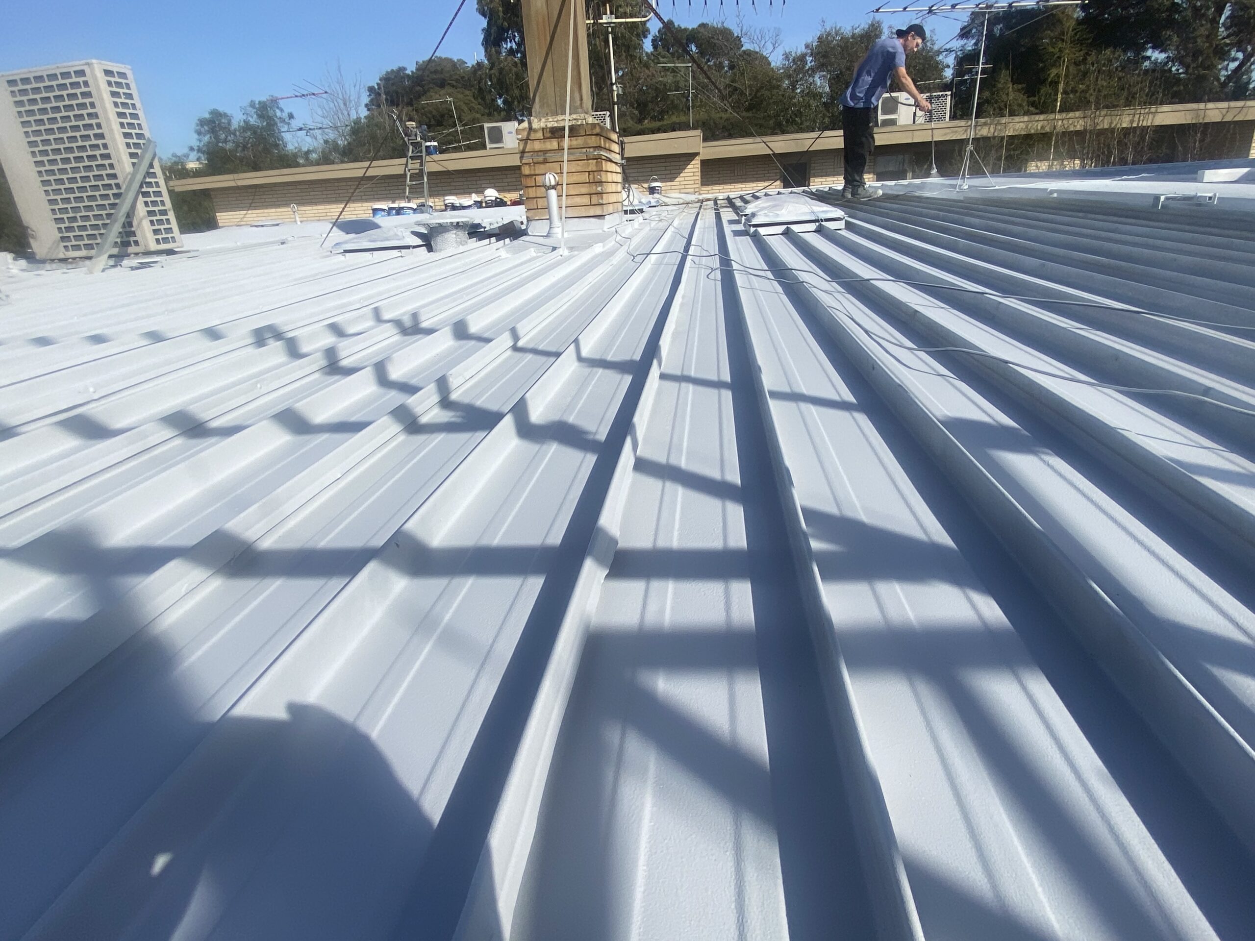 Roofing team member applying a light-coloured coating to the metal roof
