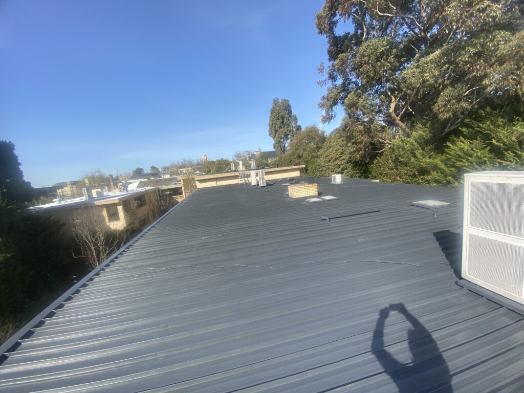 Finished dark-grey metal roof in Toorak with skylights, a chimney and air-conditioning equipment